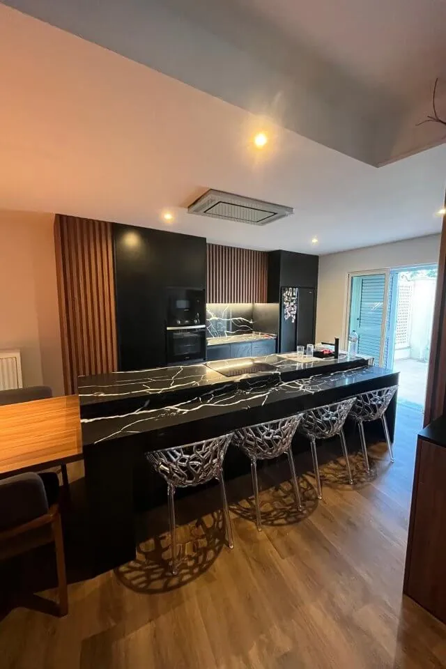 A mesma cozinha concluída, com ilha em pedra escura e bancos altos